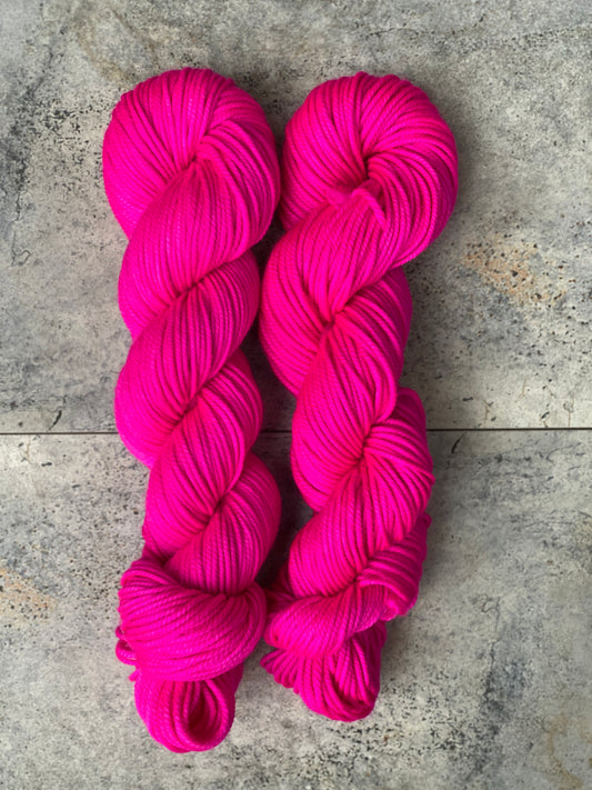 Two skeins of hot pink woolen yarn, arranged side by side on a grey background.