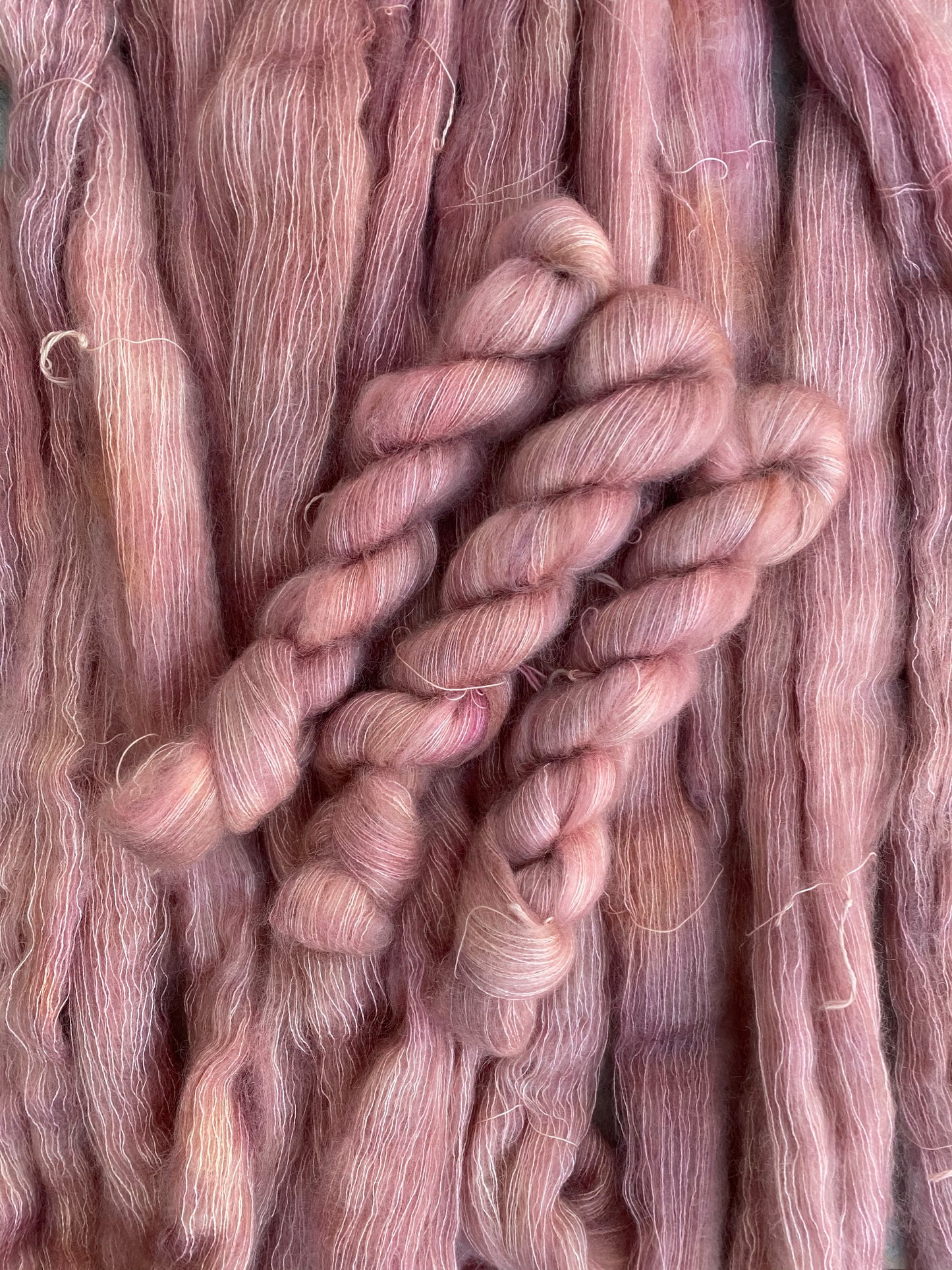 A skein of peachy pink kid mohair yarn with a lace weight texture, typically used for delicate knitting projects.