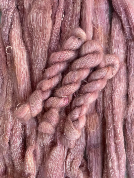 A skein of peachy pink kid mohair yarn with a lace weight texture, typically used for delicate knitting projects.