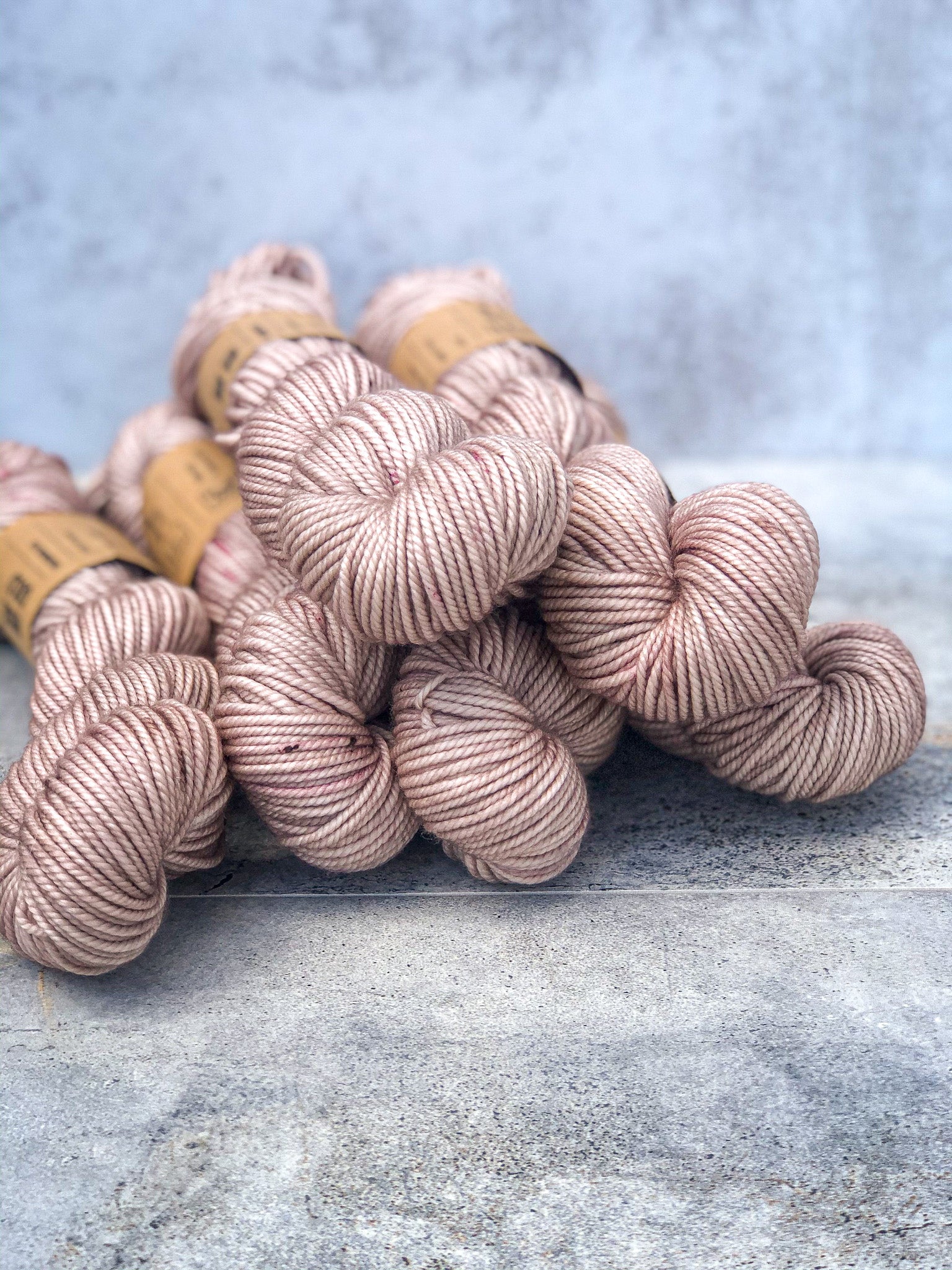 skeins of yarn in a pile dyed with a rosey gold color and pink and brown speckles, aran weight
