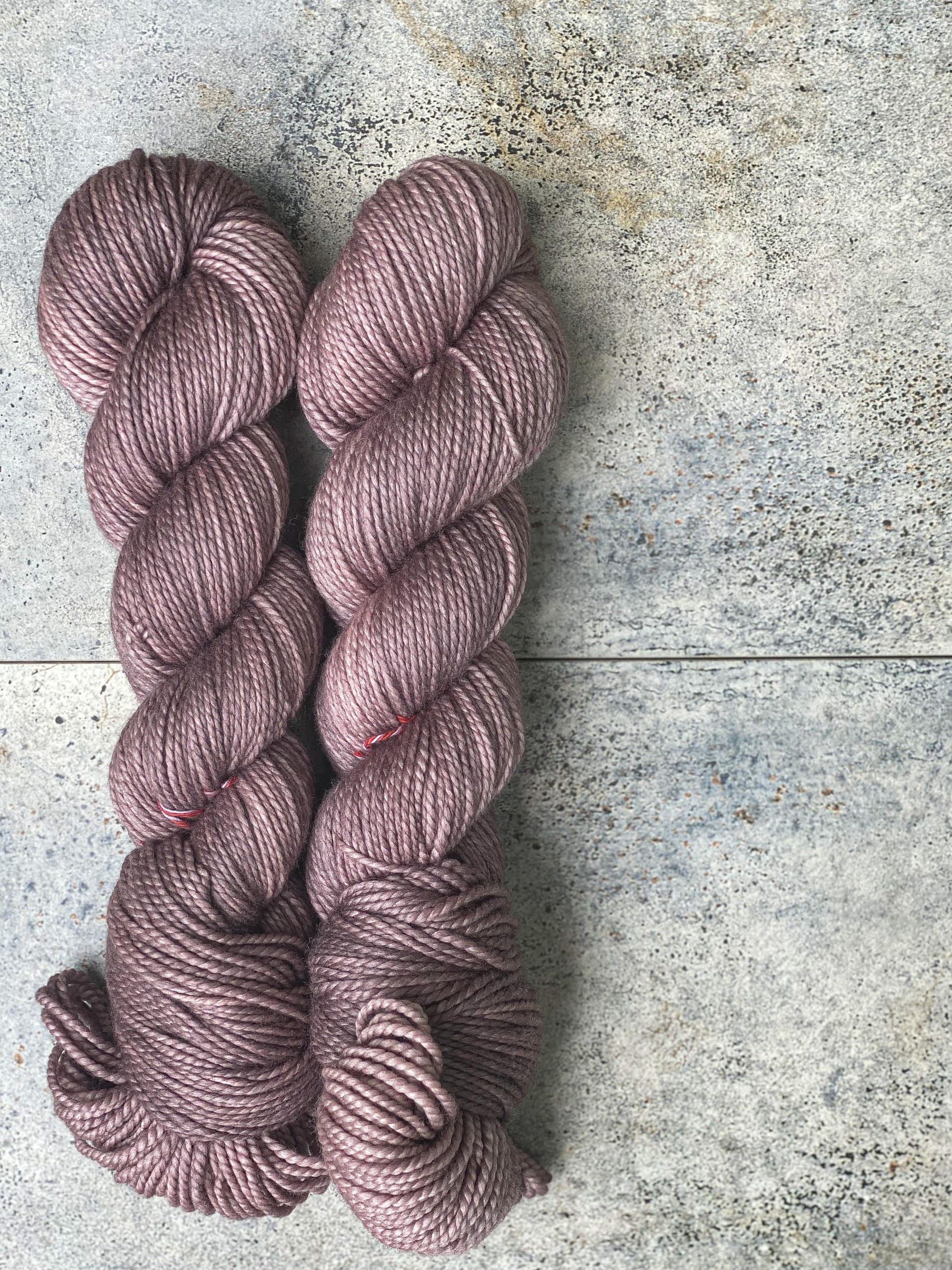 A skein of taupe-colored yarn in a worsted weight, displayed on a grey textured surface.